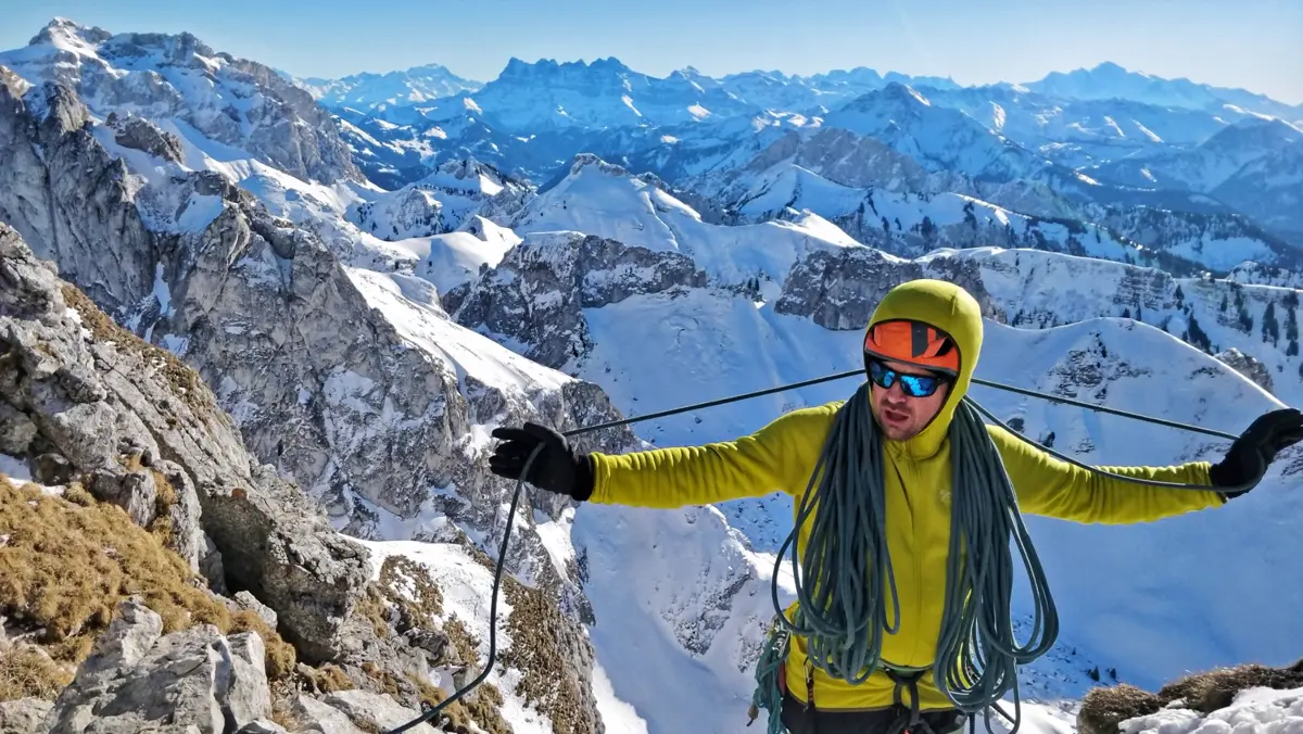 A climber coiling a rope on a snowy alpine summit with mountains behind