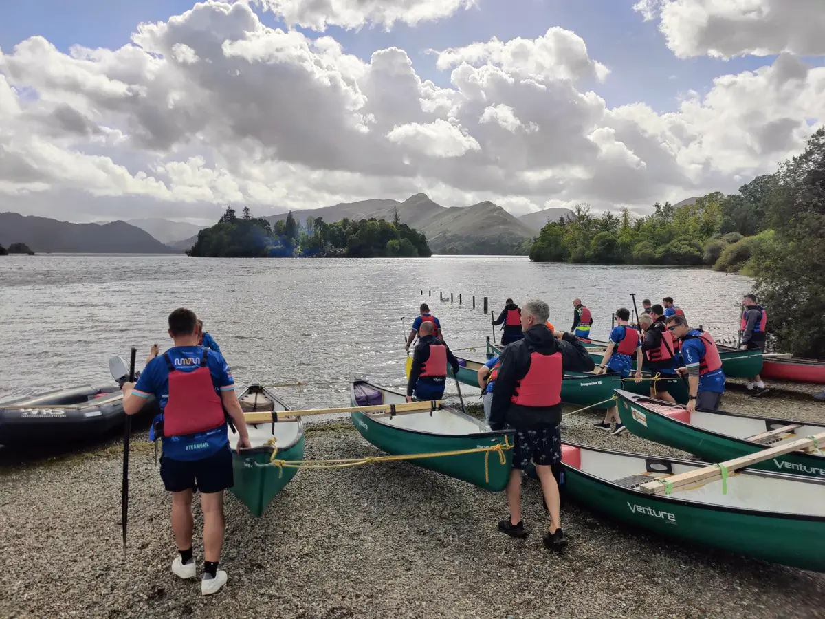 A group in buoyancy aids launching green canoes on Derwentwater in the Lake District