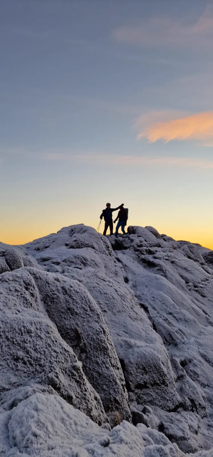 Two walkers silhouetted on a frosty summit at sunrise