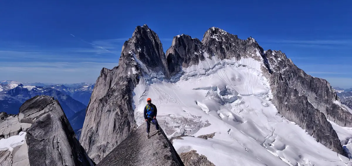A climber standing on a granite ridge in front of jagged peaks and a glacier