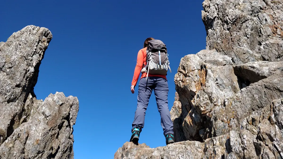 A walker with a rucksack scrambling between rock pinnacles under a deep blue sky