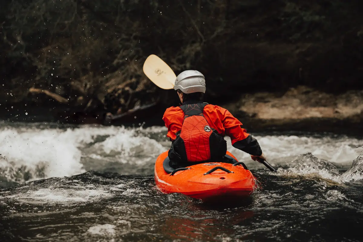 A kayaker in an orange boat paddling through white water