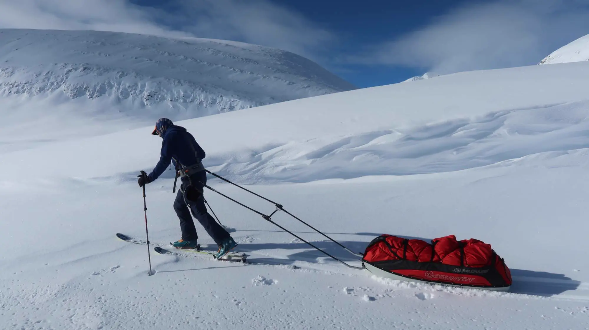Tom Shooter skiing across snow hauling a red expedition pulk